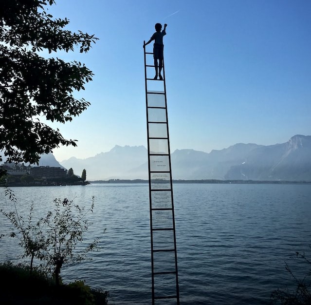 Boy standing on a ladder in a lake surrounded by mountains
